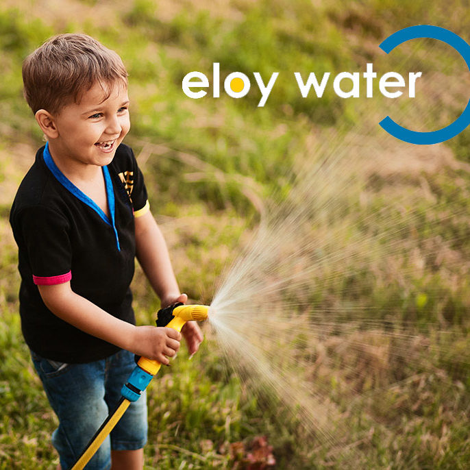 Charming little boy waters green grass on the backyard